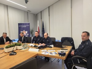 przedstawiciele Policji wraz z wójtem i przewodniczącym rady gminy siedzący przy biurku na debacie, w tle za nimi baner KPP w Krakowie (2)