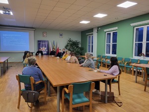 uczestnicy debaty siedzący przy stole, przed nimi policjanci, za nimi wyświetlona prezentacja oraz baner KPP Kraków