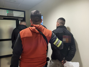 dwóch nieumundurowanych policjantów prowadzi zatrzymanego w komendzieprowadzą zatrzymanego po korytarzu budynku