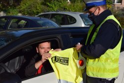 policjant przekazujący kierowcy siedzacemu w pojeździe kamizelke odblaskową