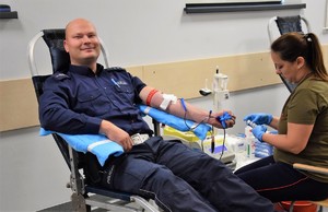 policjant podczas poboru krwi siedzący na fotelu, naprzeciwko tyłem do zdjęcia siedzi pielęgniarka