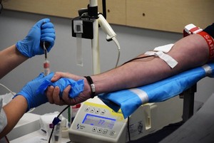 ręka z wbitą igła podczas oddawania krwi oraz ręce pielęgniarki trzymającej fiolke z krwią