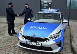 Radiowóz policyjny oznakowany, przy nim stojący Komendant Powiatowy gratuluje Komendantowi Komisariatu w Skale otrzymanego radiowozu