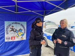 dwie policjantki przy stoisku policyjnym pod namiotem, w tle na namiocie widać logo z napisem bezpieczny powiat krakowski