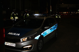 radiowóz oznakowany, wokół niego kilku policjantów, pora wieczorna