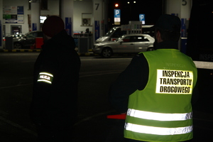 stojący tyłem nieumundurowany policjant z opaska z napisem POLICJA, obok niego stojący tyłem funkcjionariusz ITD