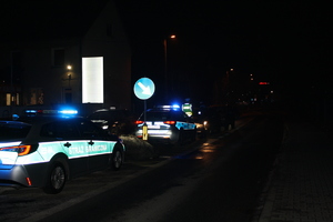 stojący pojazd Straży Granicznej, przed nim radiowóz policyjny i przed nim z koeli stojący policjant zatrzymujacy pojazdy.