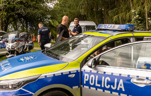 dzieci siedzące w radiowozie, w tle policjanci