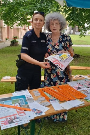 policjantka z kobietą stoją przy stoisku policyjnym wypełnionym ulotkami i odblaskami