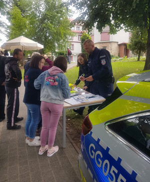 dwoje policjantów przy stoisku policyjnym, przed nimi osoby biorące odblaski (2)