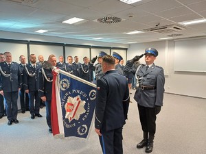 mł. insp. Jacek Rosół  oraz insp. Jacek Cholewa stoją przy sztandarze Komendy Powiatowej Policji w Krakowie, naprzweciwo siebie (2)