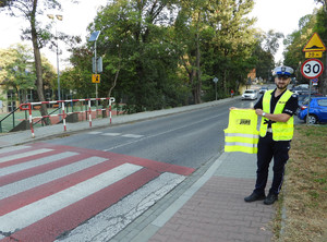 policjant trzymający w ręku kamizelkę odblaskową przy przejściu dla pieszych