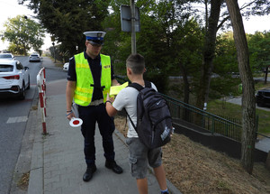 policjant wręczajacy dziecku kamizelkę odblaskową