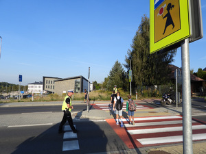 dwoje policjantów stojących przy przejściu dla pieszych po obu stronach ulicy przed szkołą, dzieci przechodzące przez jezdnię, stojący motocykl przed przejściem