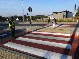 dwoje policjantów stojących przy przejściu dla pieszych po obu stronach ulicy przed szkołą, dziecko przechodzące po przejściu