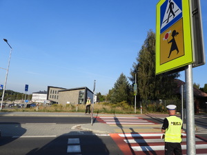 dwoje policjantów stojących przy przejściu dla pieszych po obu stronach ulicy przed szkołą