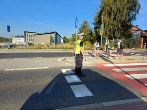 policjanci stojący przy przejściu dla pieszych po obu stronach jezdni i przechodzace dzieci przez pasy