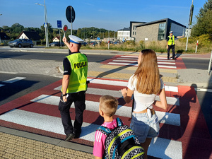 policjant z podniesionym lizakiem, przeprowadzający dzieci przez przejście dla pieszych