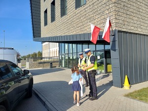 policjanci stojący przed wejściem do szkoły przekazują odblask dziewczynce