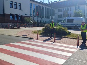 policjanci stojący przy przejściu dla pieszych, w tle szkoła i zaparkowany radiowóz