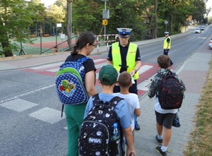 policjant rozdający przy pasach kamizelki odblaskowe