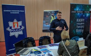 Policjant przy stoisku promocyjnym służby w policji rozmawiający z uczestnikiem targów