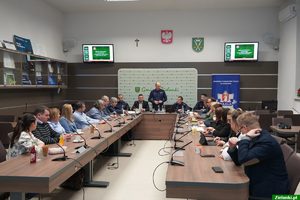 uczestnicy debaty siedzący przy stołach, w tle przedstawiciele Policji