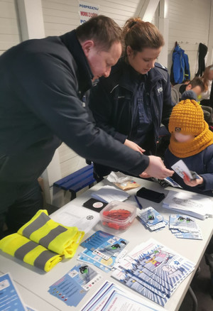 dwoje policjantów przy policyjnym stoisku na terenie lodowiska, wręczają dziecku ulotkę