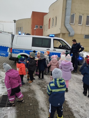 dzieci stojące przed radiowozem, obok policjant