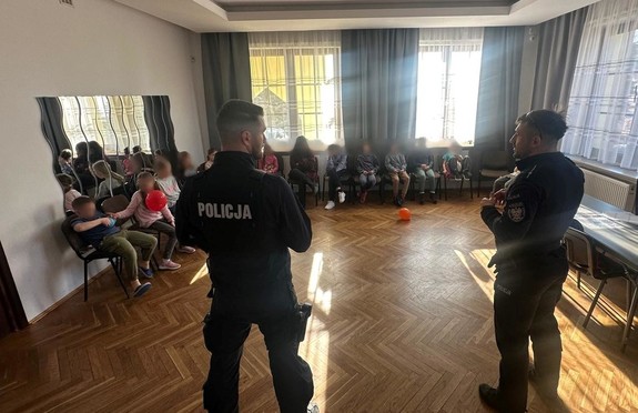 dwóch policjantów stojących tyłem do zdjecia przed nimi grupa siedzących na krzesłach dzieci (1)