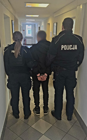 dwoje policjantów prowadzących po korytarzu komisariatu zatrzymanego z kajdankami na ręce trzymane z tyłu (2)