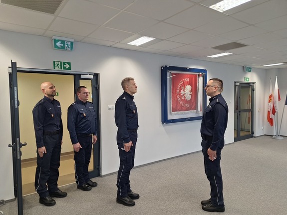 Czterech policjantów w mundurze stoi na baczność