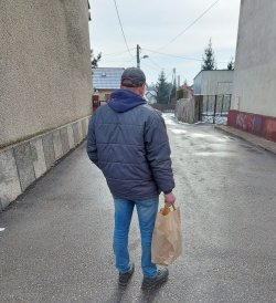 mężczyzna stojący tyłem z reklamówką jedzenia, którą dostał od policjantek