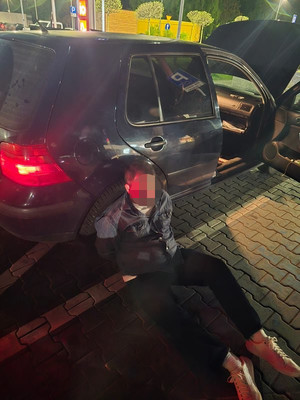 zatrzymany mężczyzna siedzący na ziemi oparty o niebieski samochód.jpg