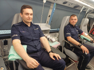 Dwóch umundurowanych policjantów siedzących w autobusie policjant po prawej stronie oddaje krew