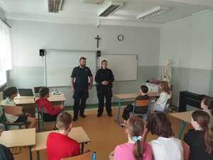 umundurowany policjant i policjantka stoją w klasie lekcyjnej przed dziecmi