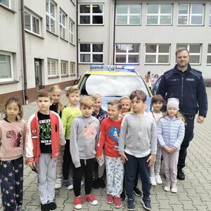umundurowany policjant stojący wspólnie z dziećmi przed oznakowanym radiowozem