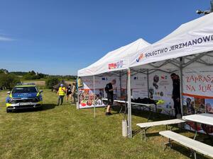 oznakowany radiowóz, obok policyjne stoisko pod namiotem