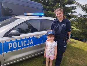 umundurowana policjantka stoi przed radiowozem z dziewczynką w policyjnej czapce