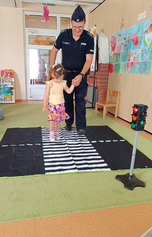 umundurowany policjant z dziewczynką przechodzą przez ćwiczebne przejście dla pieszych