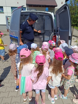 umundurowany policjant pokazuje dzieciom radiowóz