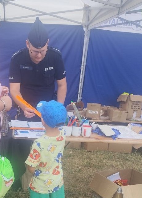 umundurowany policjant na stoisku profilaktycznym z dzieckiem