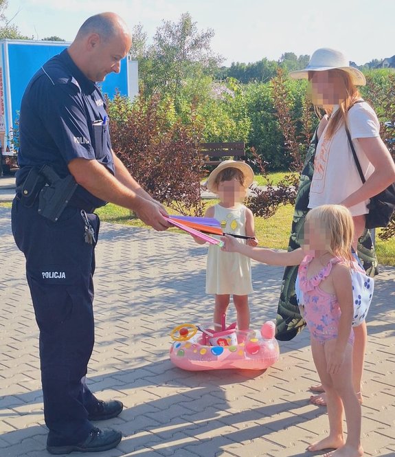 umundurowany policjant wręcza dziewczynkom odblaski