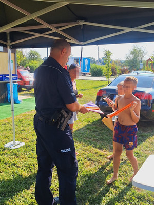 umundurowany policjant pod namiotem z dziećmi , którym przekazuje odblaski
