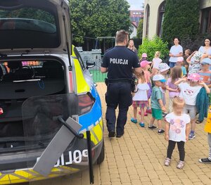 umundurowany policjant stojący przed dziećmi obok radiowozu