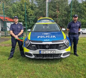 dwóch umundurowanych policjantów stojących przy oznakowanym radiowozie