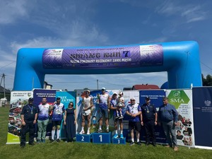 zwycięzcy biegu stojący na podium wspóknie z organizatorami biegu