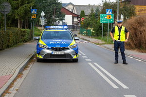 oznakowany radiowóz i umundurowany policjant na drodze
