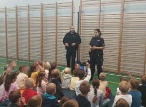 umundurowana policjantka i policjant przed nimi siedzą dzieci podczas pogadanki na sali gimnastycznej