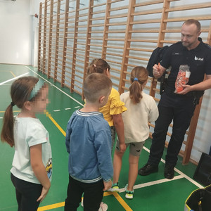 umundurowany policjant rozdaje dzieciom odblaski